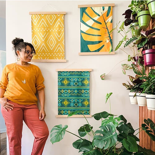 woman standing in her living room next to three custom-printed tropical-themed wall hangings and a display of text