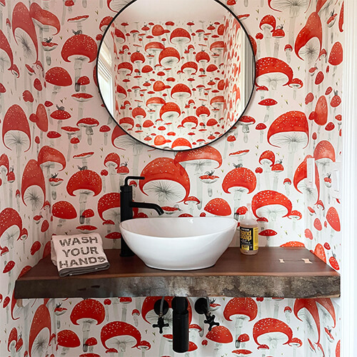 a bathroom covered with mushroom wallpaper and a wooden countertop and round mirror