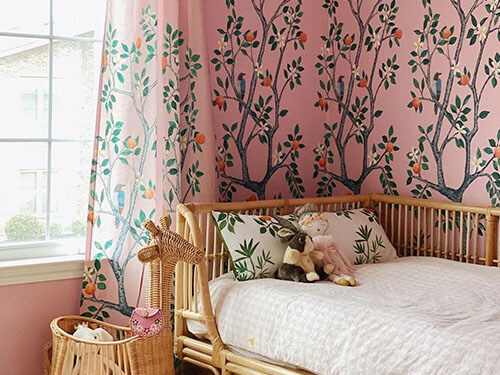 Pink wallpaper with branches, trees and oranges with matching curtains in a child's bedroom