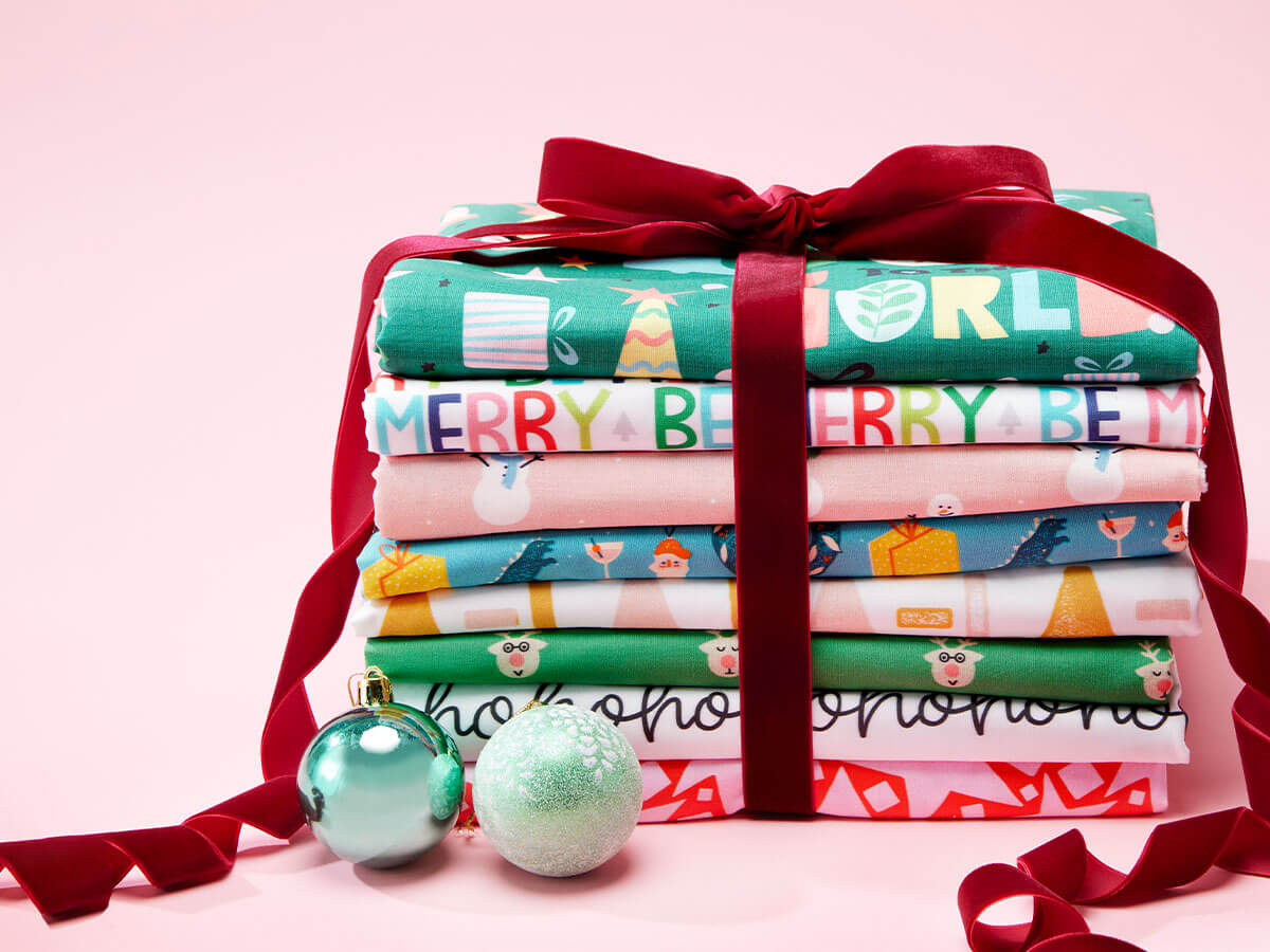 stack of holiday themed fabric styled to look like a gift with a velvet ribbon tied around the stack.